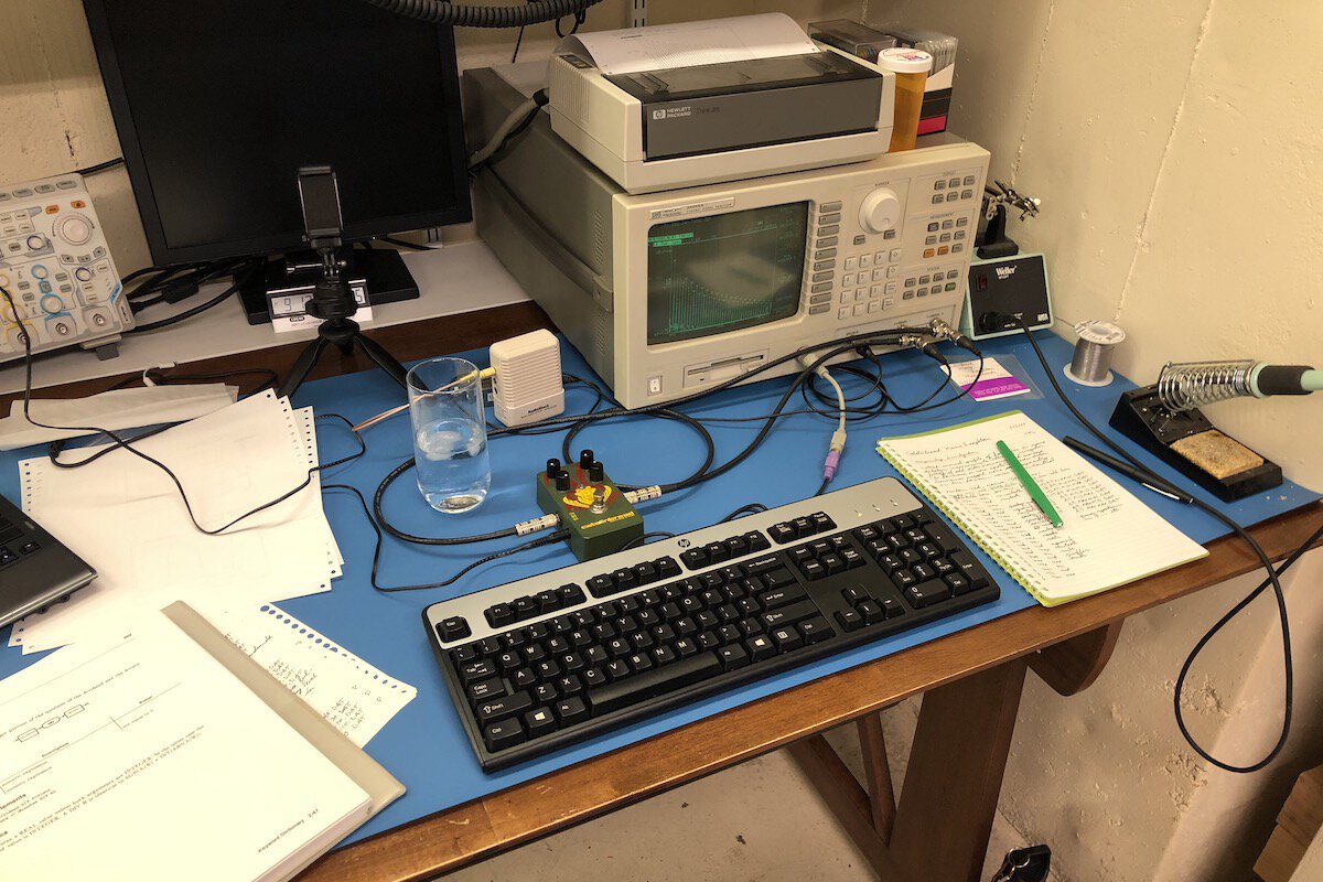 A Catalinbread Manx Loaghtan guitar effect pedal sits on an electronics
work bench connected to a dynamic signal analyzer. Also visible are a manual
for the DSA, a glass of water, keyboard, soldering iron, and some hand-written
notes.