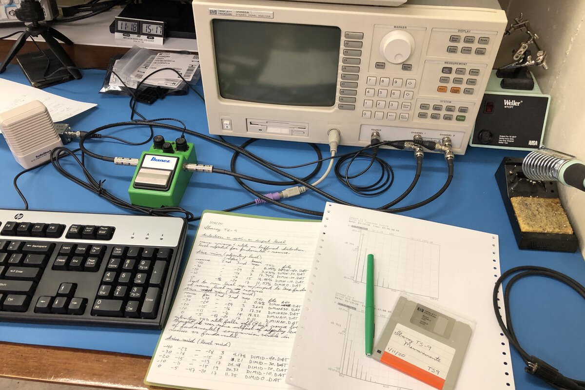 An Ibanez TS-9 guitar pedal sits on an electronics workbench in front of a
dynamic signal analyzer. A notebook, some printouts, and a floppy disk can be
seen in the foreground.
