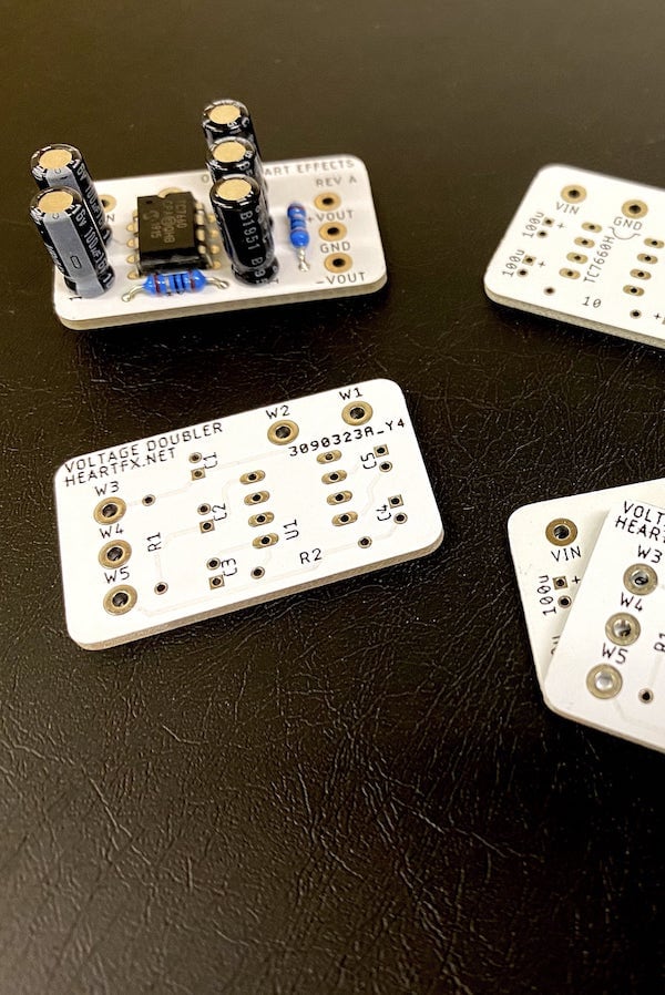 Several small
white circuit boards sit on a black card table. One is assembled with
electrolytic capacitors, a couple of resistors, and an eight-pin DIP chip.