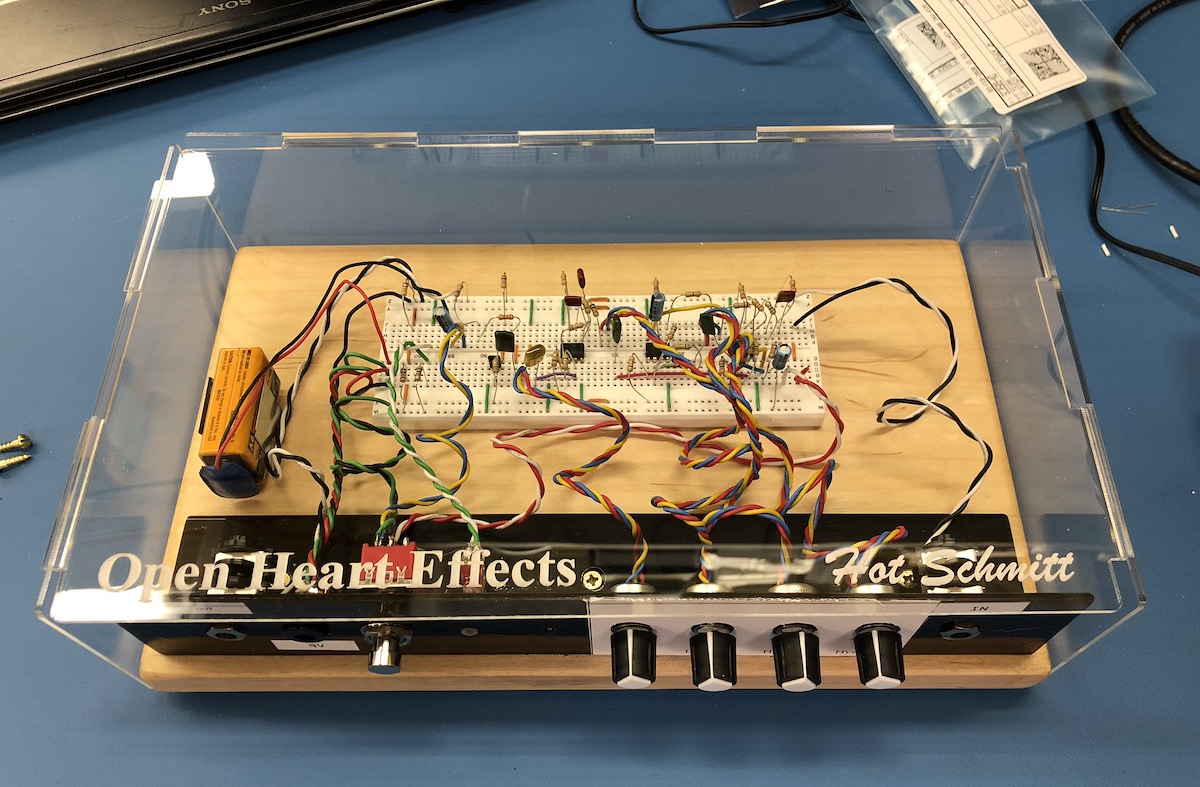 A prototype guitar
effect sits on an anti-static mat. It's built on a plank of clear-finished maple
with the electronic components assembled onto a single 3M SuperStrip board.
Adjustments and controls are mounted in a length of aluminum angle which has
been painted black. They connect to the SuperStrip via multi-colored wires.
While the maple plank makes up the bottom of the assembly and the aluminum angle
forms the front, the remaining four sides are enclosed by clear acrylic sheet.
The acrylic sheet is laser-engraged with the words 'Open Heart Effects' and 'Hot
Schmitt'