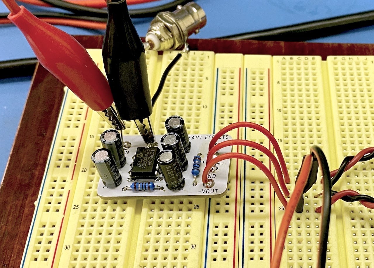 A small white
printed circuit board surmounts a beige spring-contact breadboard. A pair of
black and red alligator clips connect to its power input while three red
wires connect its power output to the breadboard.